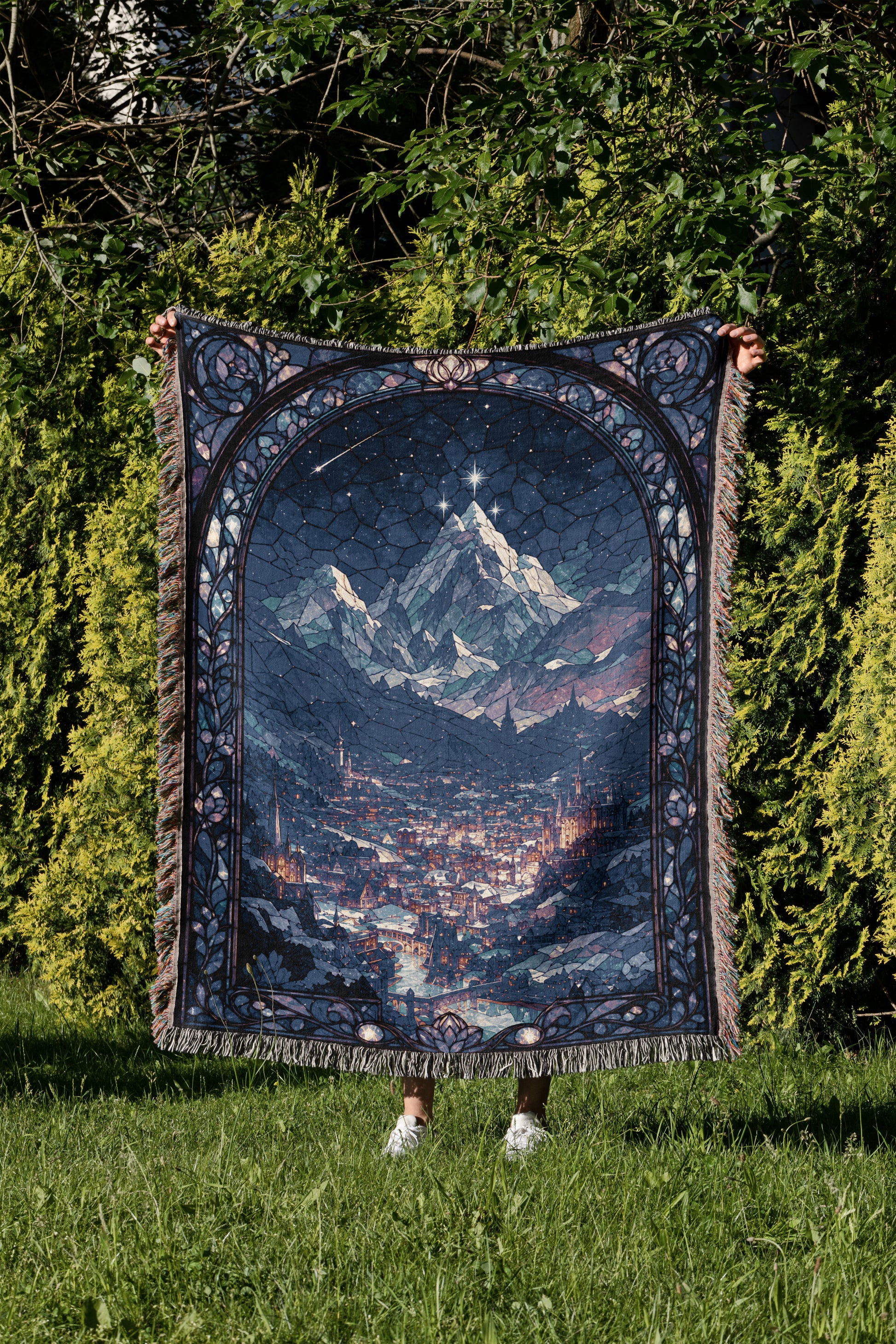 A person is holding up a large, intricately designed tapestry depicting a mountainous landscape with a starry night sky.