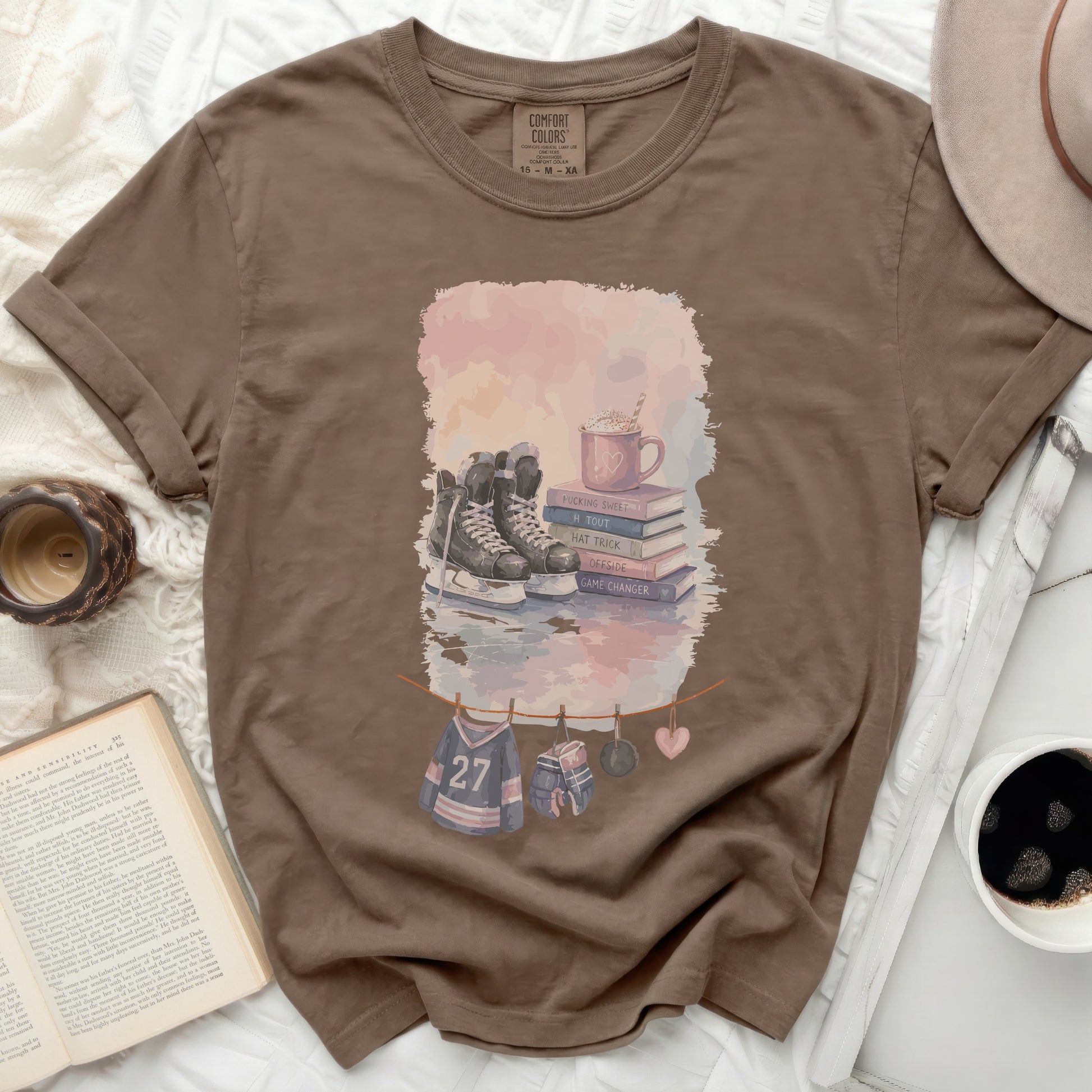Brown Comfort Colors t-shirt with ice skates, hockey gear, and book illustrations.