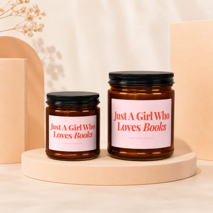 Two amber glass candles with black lids feature pink labels saying "Just A Girl Who Loves Books."