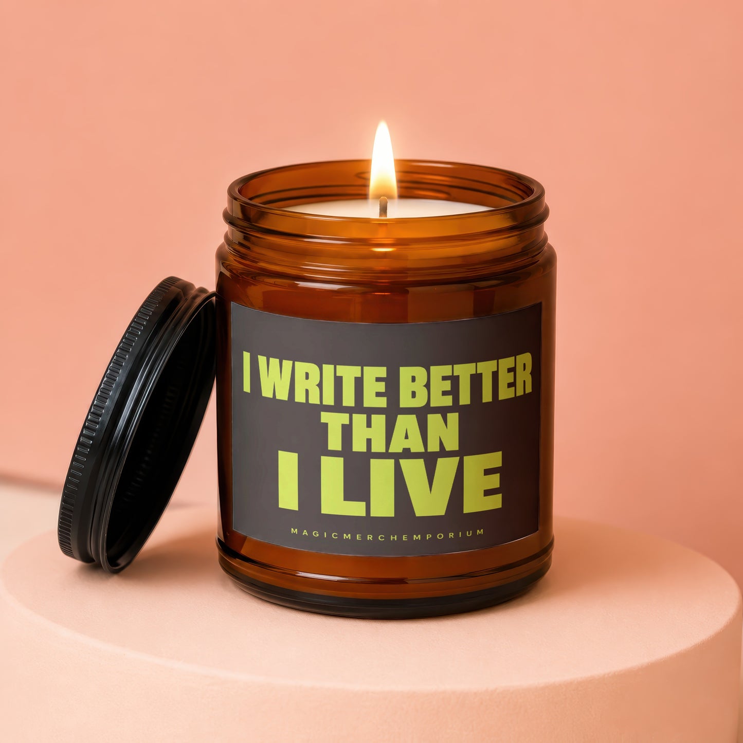 Amber jar candle with lid off, lit flame, reading "I WRITE BETTER THAN I LIVE"