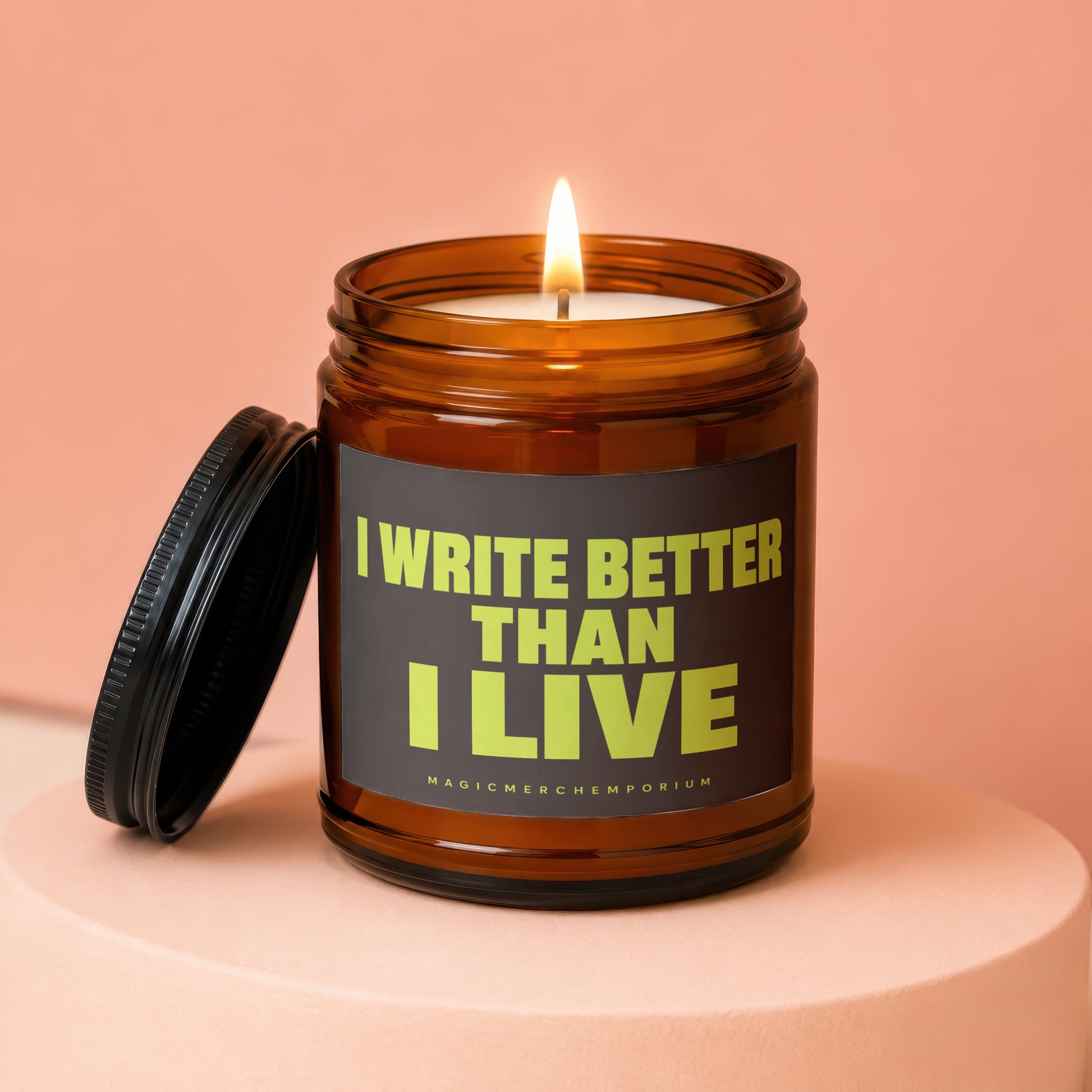 Amber jar candle with lid off, lit flame, reading "I WRITE BETTER THAN I LIVE"