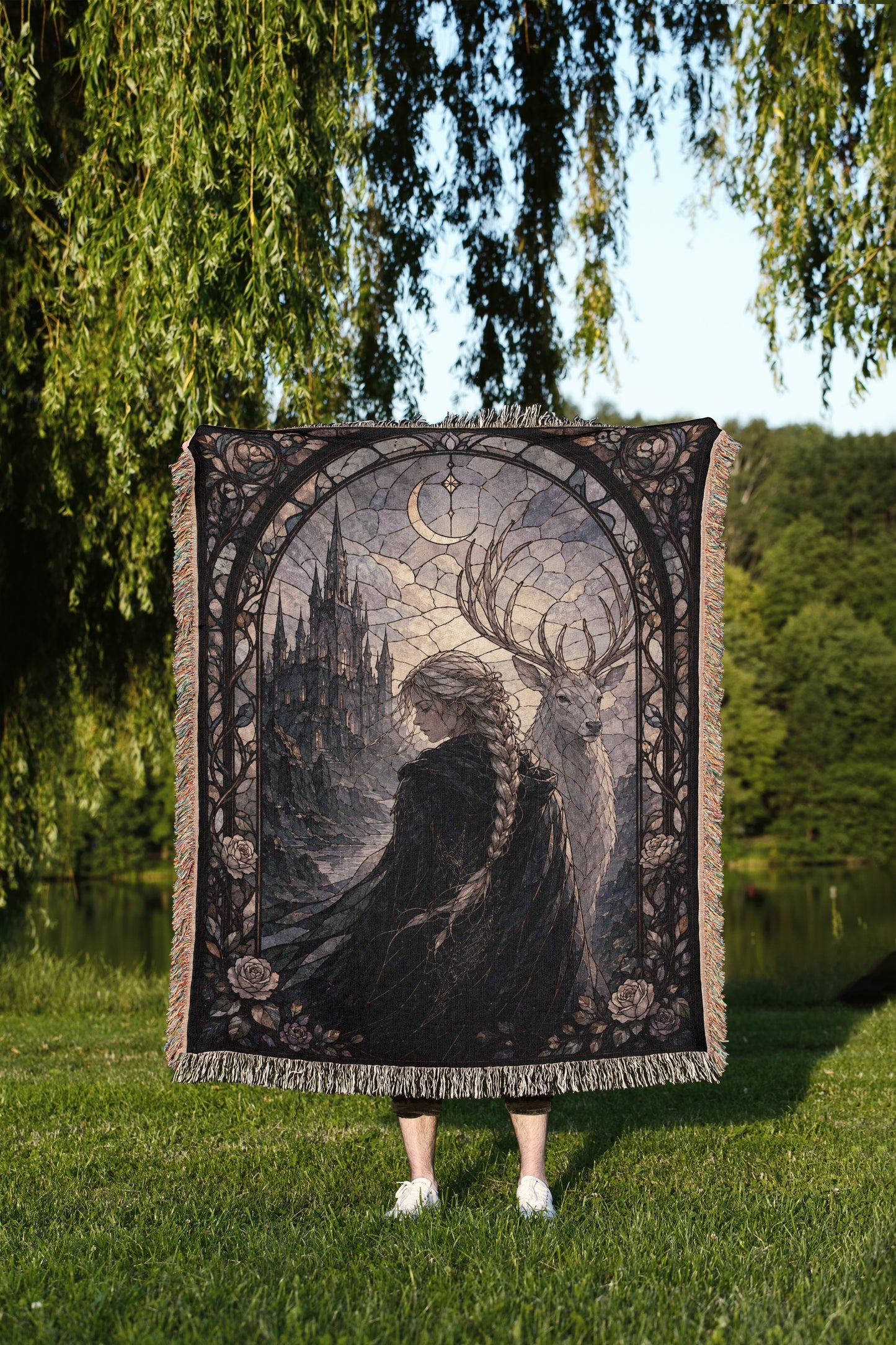 A person is standing in a grassy area, holding a large tapestry or blanket that features a detailed illustration of a woman with a castle in the background.