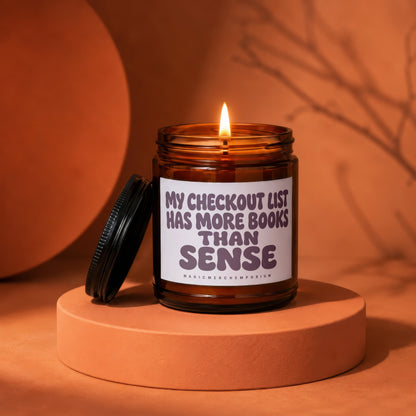 Amber glass candle with lit wick and text "My checkout list has more books than sense".