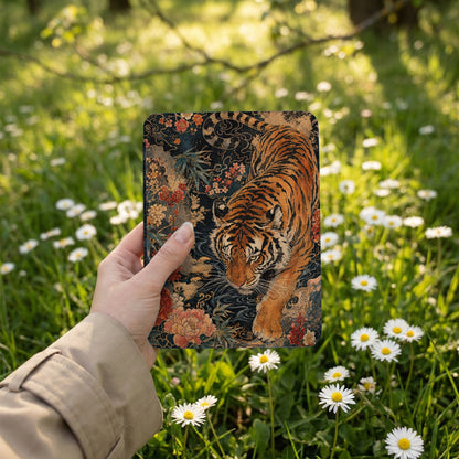 Tiger art on a patterned background held by a hand outdoors among daisies.
