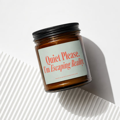 Amber jar candle with a cream label reading "Quiet Please. I;m Escaping Reality."