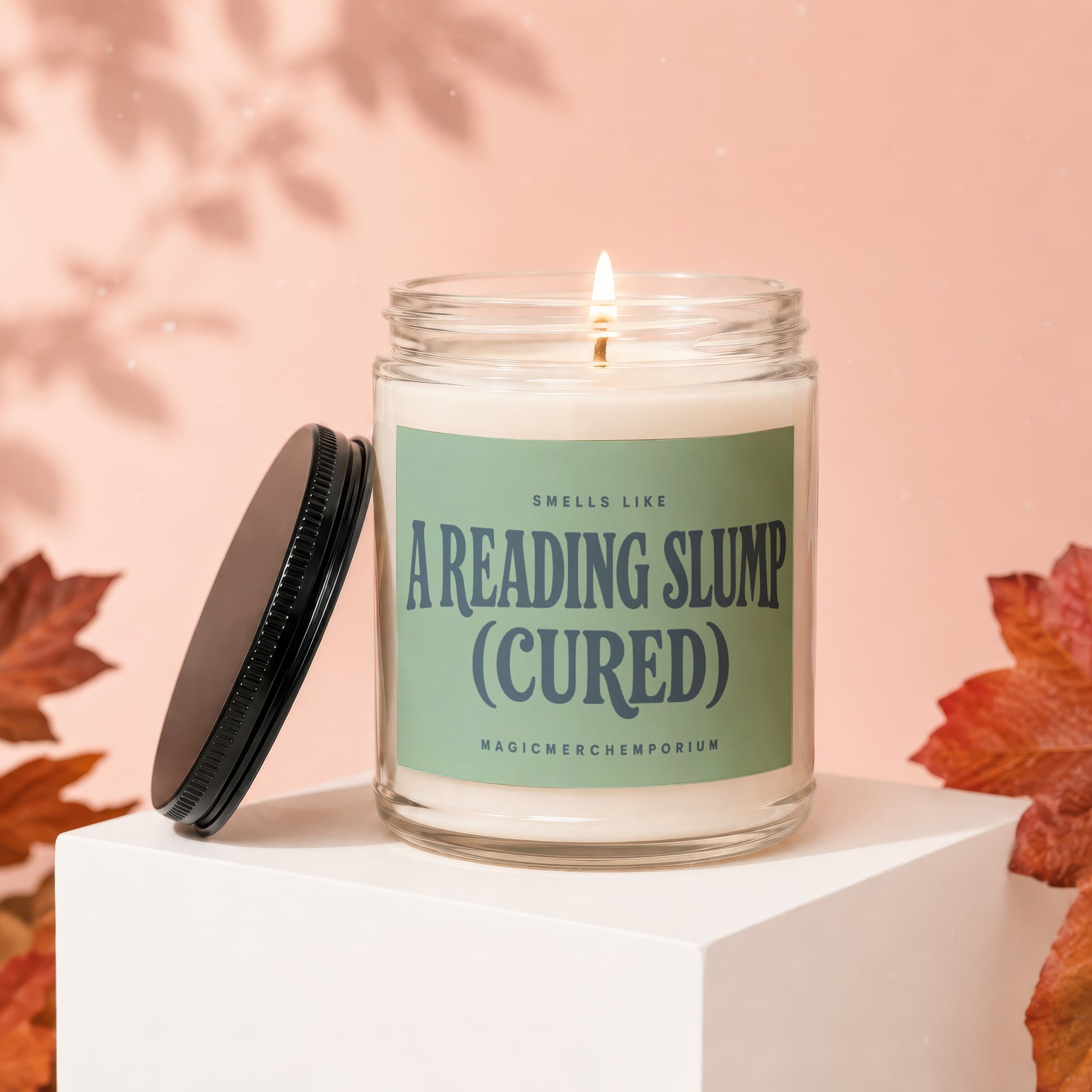 Glass candle with a lit wick, label reads "Smells Like A Reading Slump (Cured)".