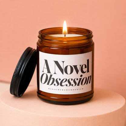 Amber jar candle with lit wick, lid off, reading "A Novel Obsession"