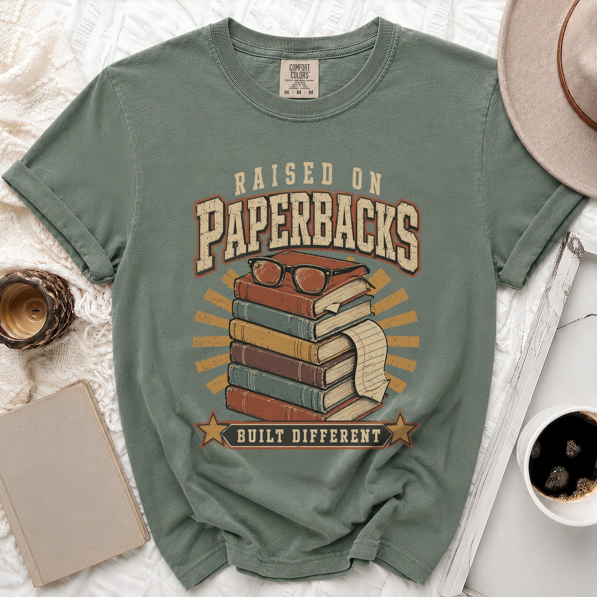 Green t-shirt with "Raised on Paperbacks Built Different" text and stack of books graphic.