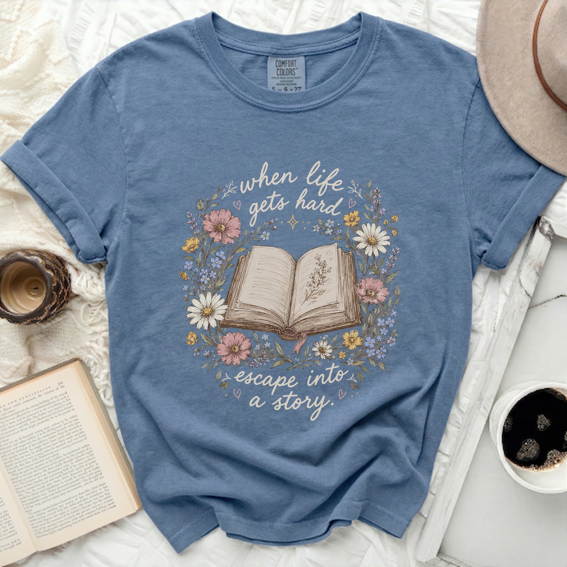 Blue t-shirt with open book and floral wreath, "when life gets hard escape into a story."