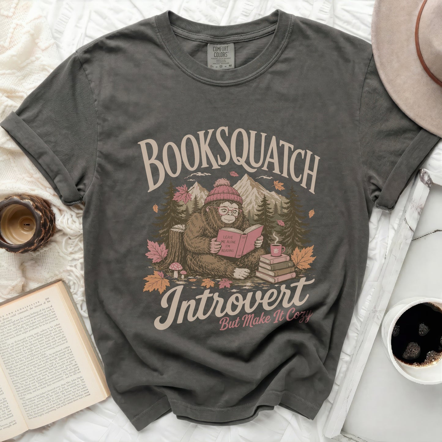 Graphic t-shirt with a Bigfoot reading a book, "Booksquatch Introvert" text.