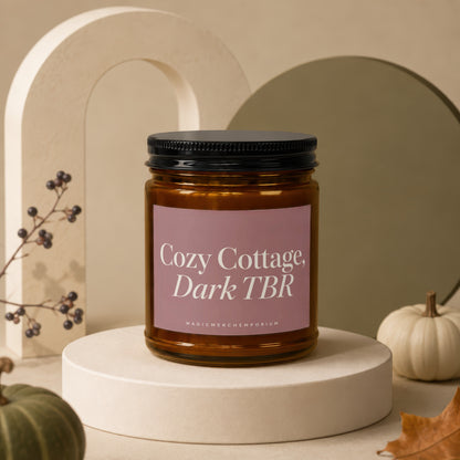 Amber candle with a pink label reading "Cozy Cottage, Dark TBR".