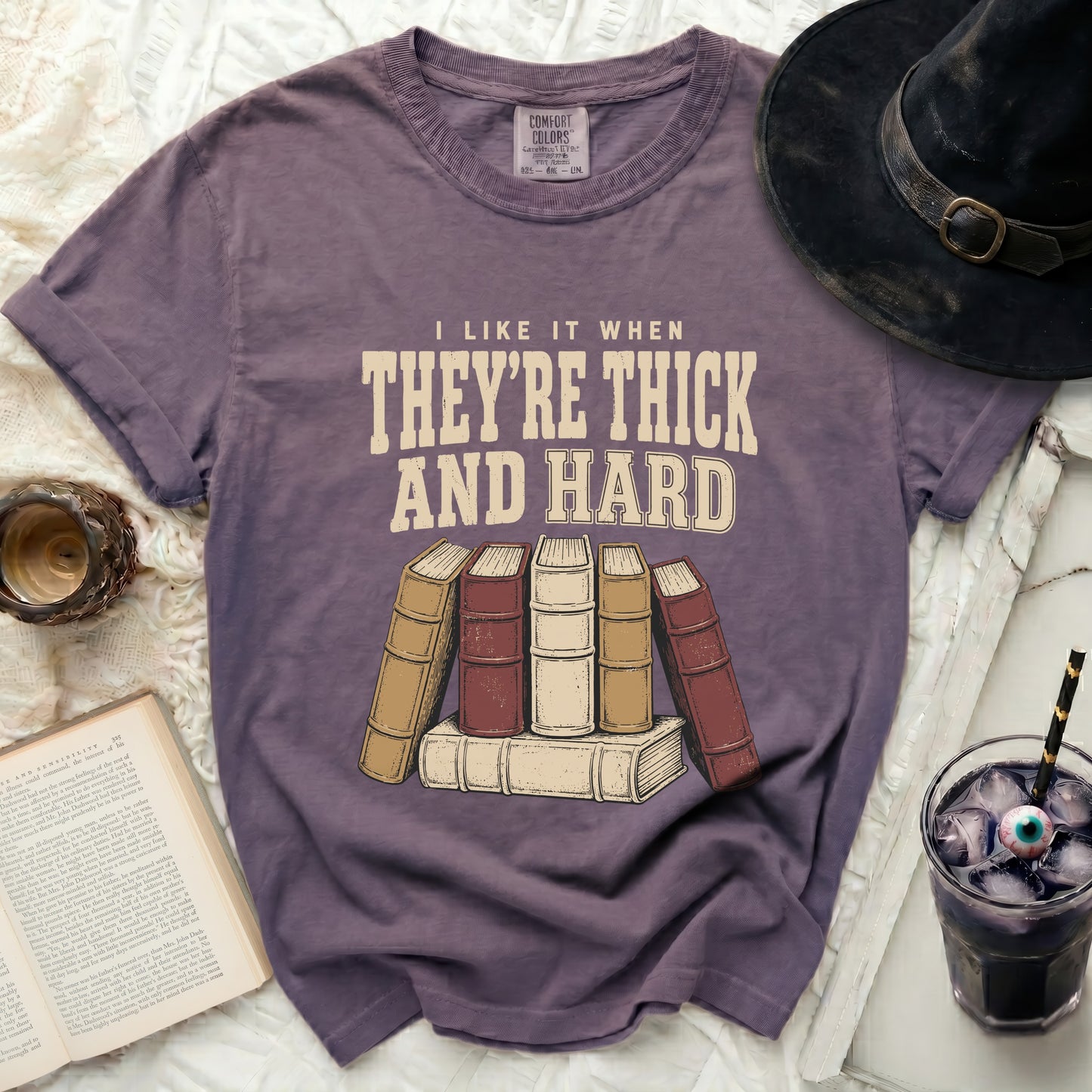 Purple t-shirt with "I like it when they're thick and hard" text and stacked books.