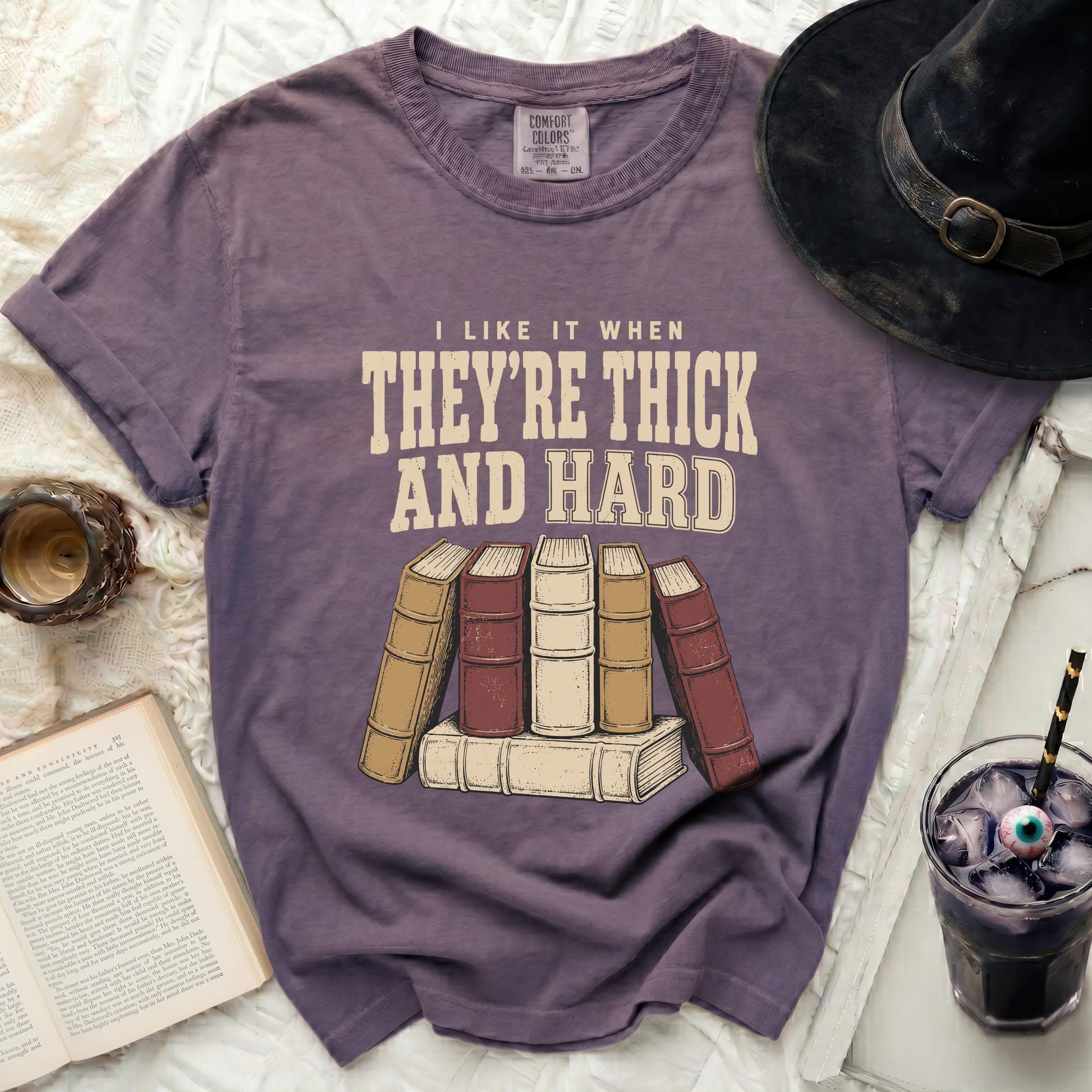 Purple t-shirt with "I like it when they're thick and hard" text and stacked books.
