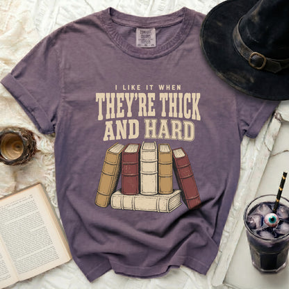 Purple t-shirt with "I like it when they're thick and hard" text and stacked books.
