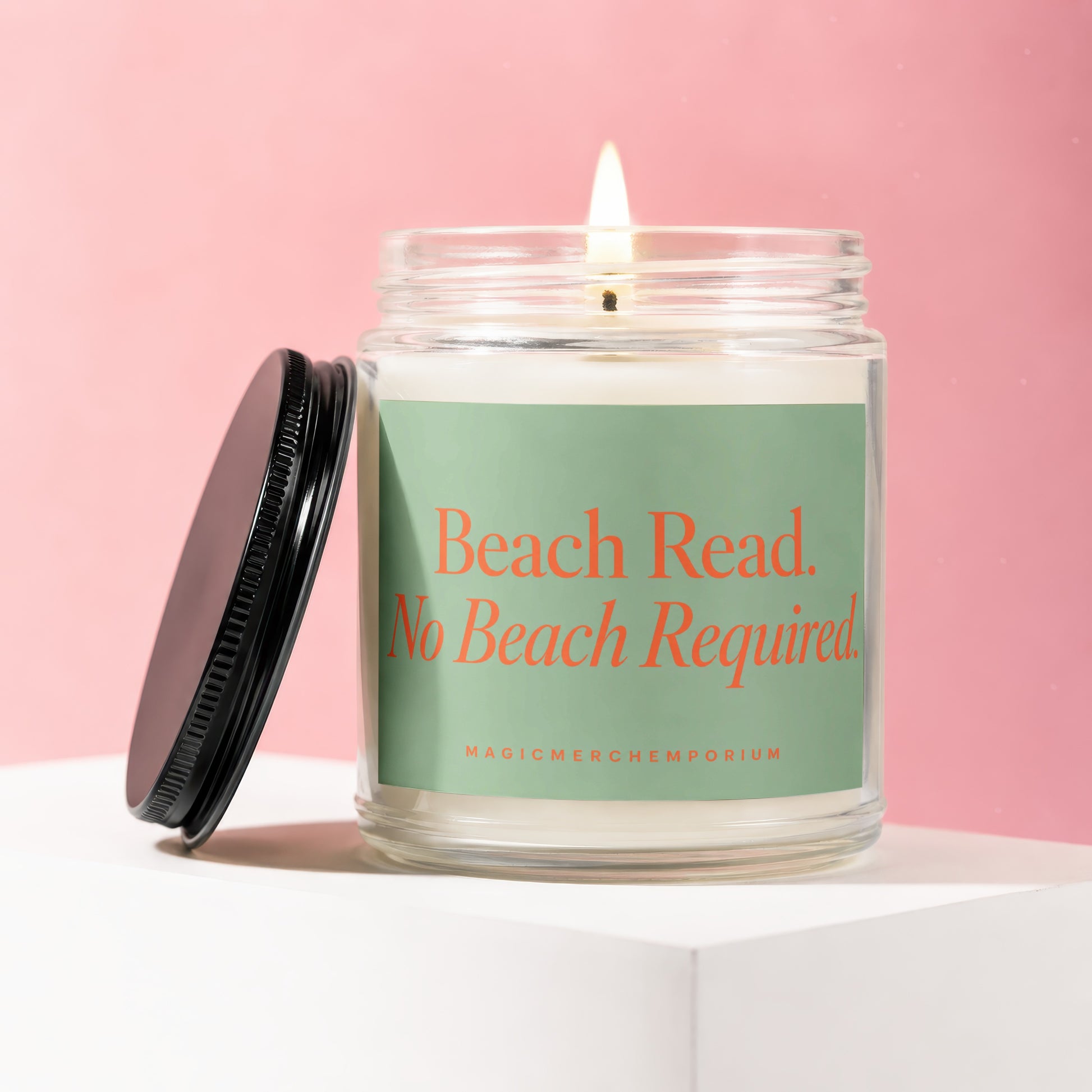 Glass candle with lit wick and lid off, displaying text "Beach Read. No Beach Required."