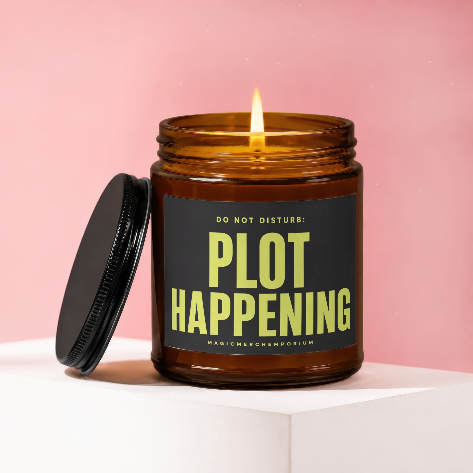 Lit amber glass candle with black lid and label that reads "DO NOT DISTURB: PLOT HAPPENING".