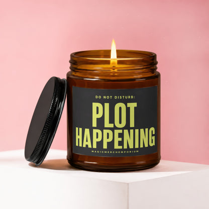 Lit amber glass candle with black lid and label that reads "DO NOT DISTURB: PLOT HAPPENING".