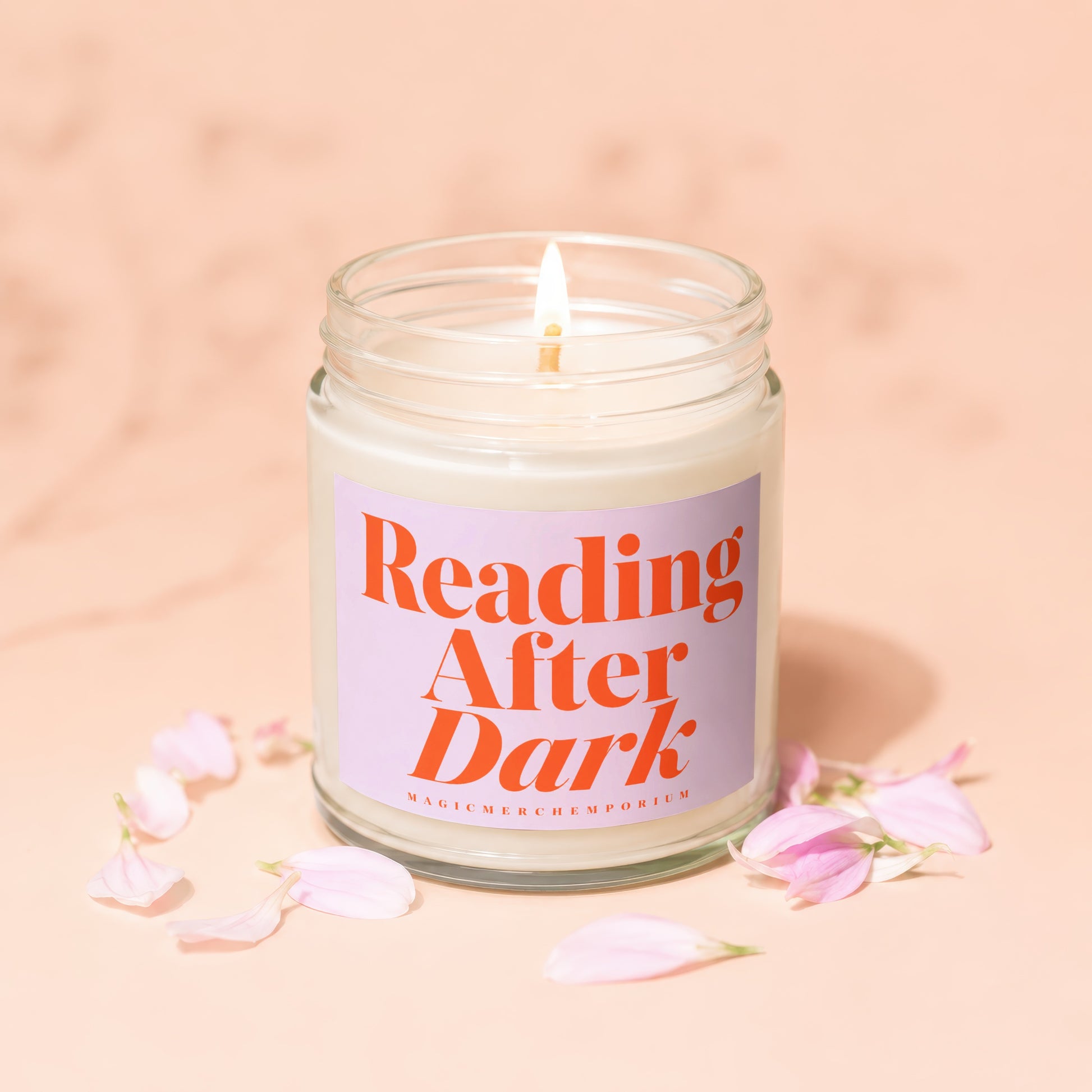 Lit "Reading After Dark" candle surrounded by pink flower petals.