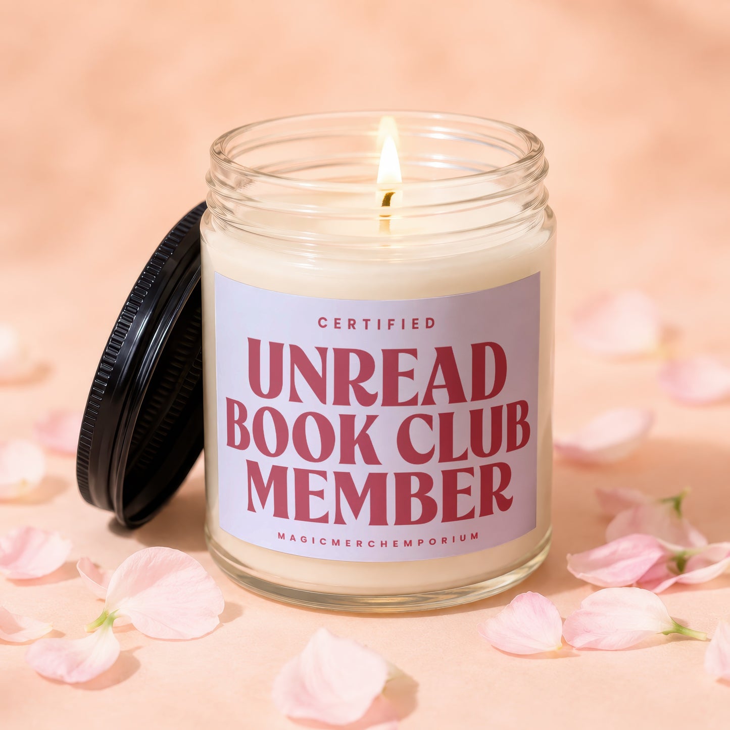 Lit glass candle with "Certified Unread Book Club Member" label surrounded by pink petals.