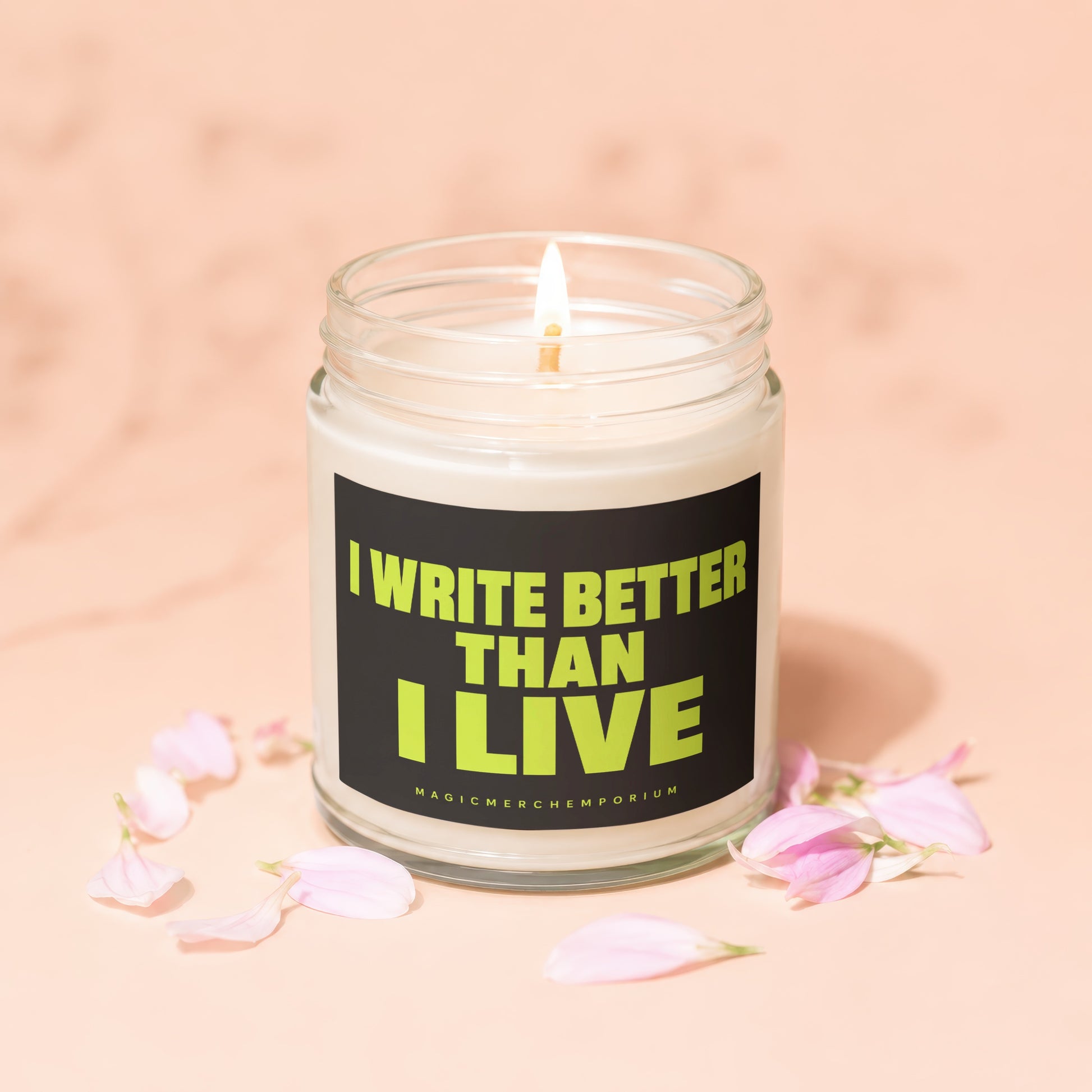 Lit candle in glass jar with "I WRITE BETTER THAN I LIVE" text and flower petals.