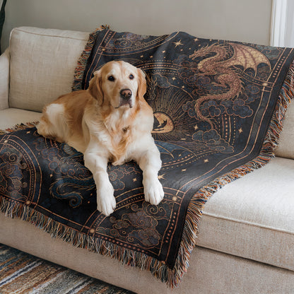 A golden retriever dog is sitting on a couch, resting on a decorative blanket with a dragon design.
