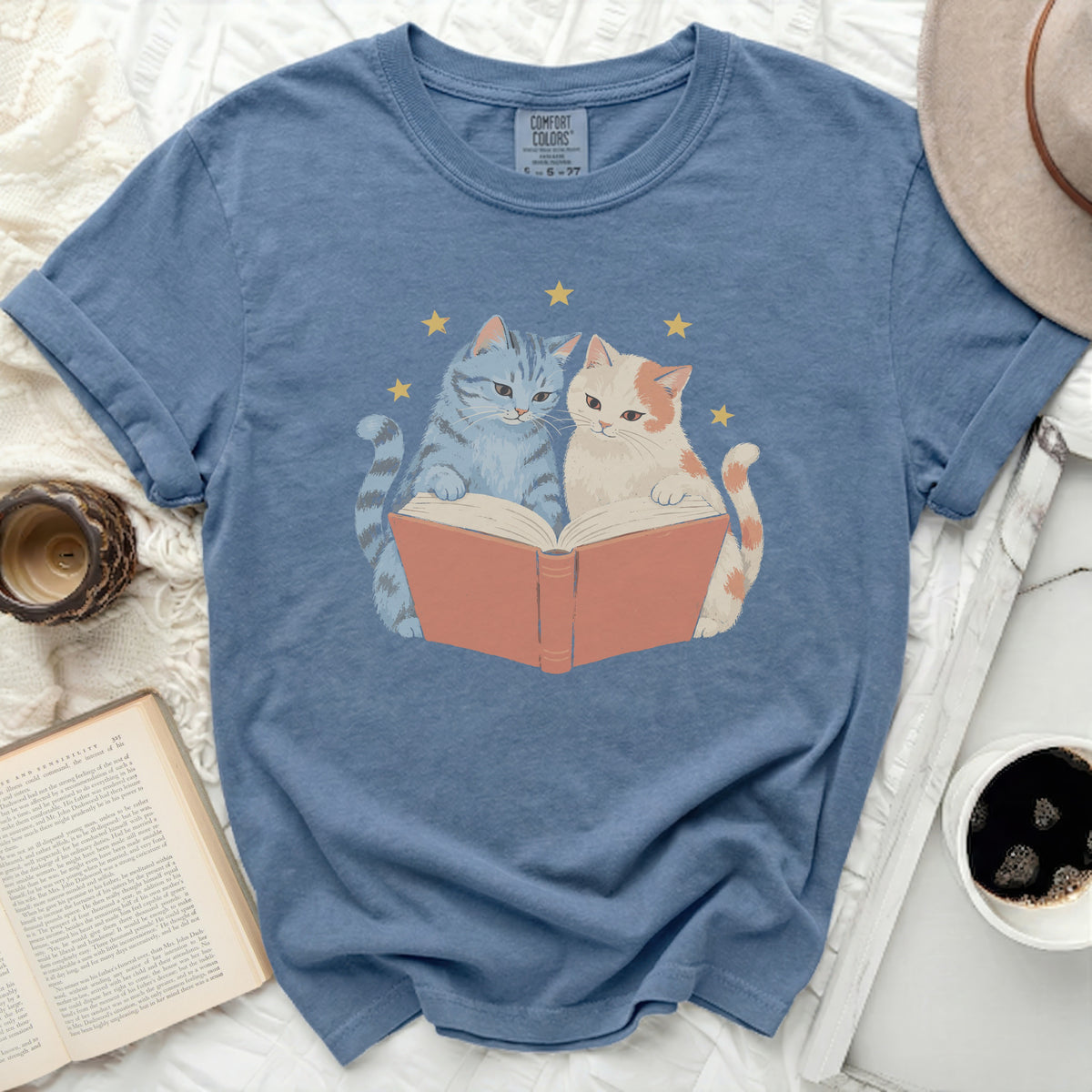 Blue t-shirt with blue and white cats reading a book, surrounded by stars.