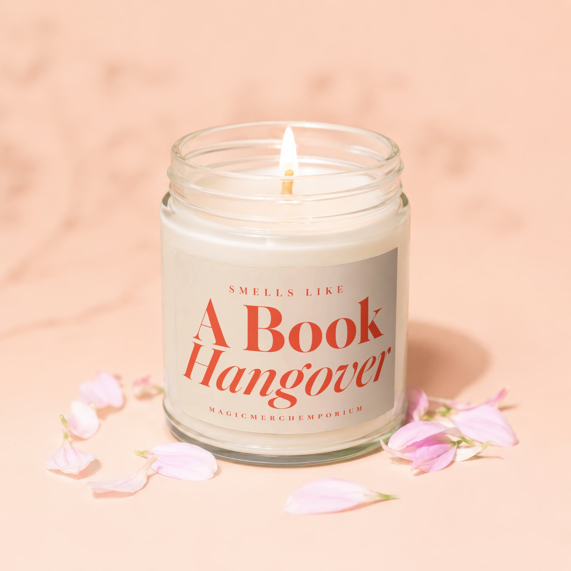 Scented candle in glass jar with lit wick and pink petals, labeled "A Book Hangover".