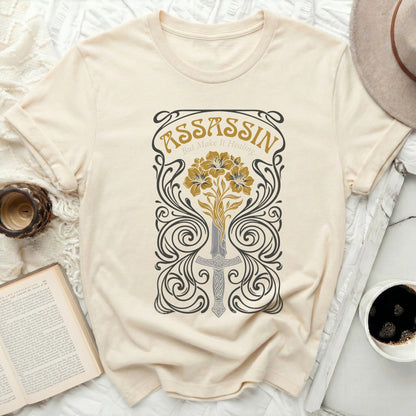 Cream t-shirt with a sword, flowers, and "Assassin But Make It Healing" text.