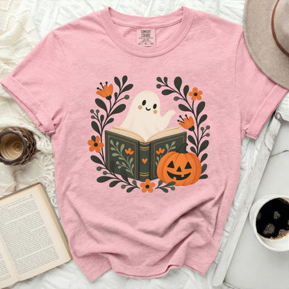 Pink t-shirt with a graphic of a ghost reading a book surrounded by pumpkins and flowers.