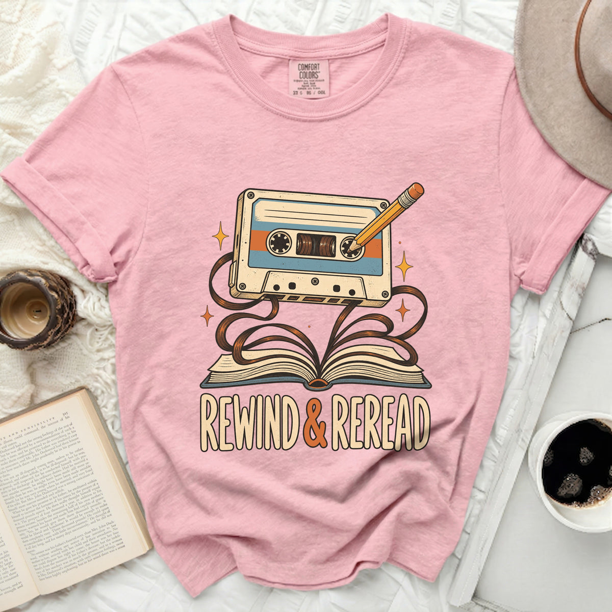 Pink t-shirt with retro cassette, pencil, and "REWIND & REREAD" text graphic.