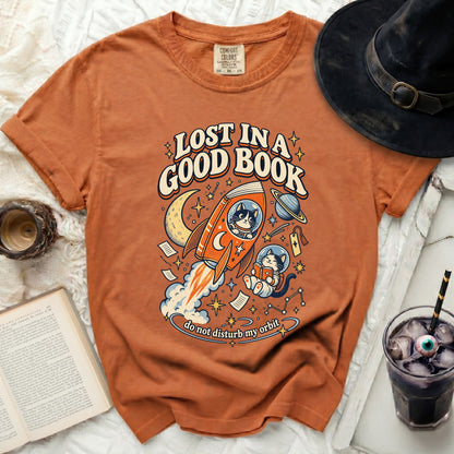 Orange t-shirt with graphic of cats in space with text "LOST IN A GOOD BOOK".