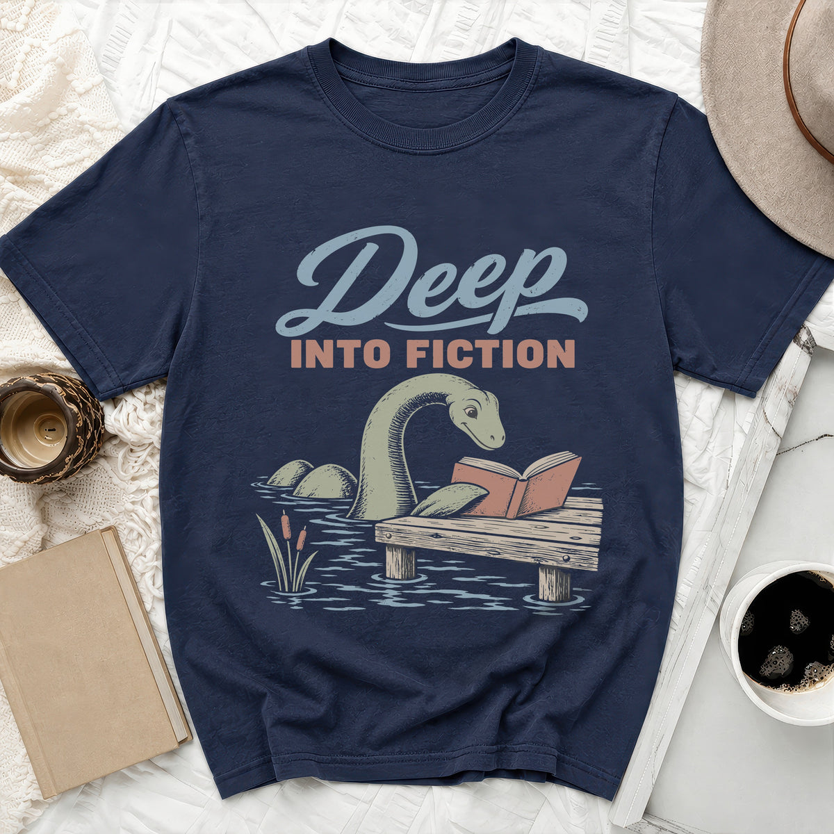 Navy t-shirt with a loch ness monster reading a book on a dock.