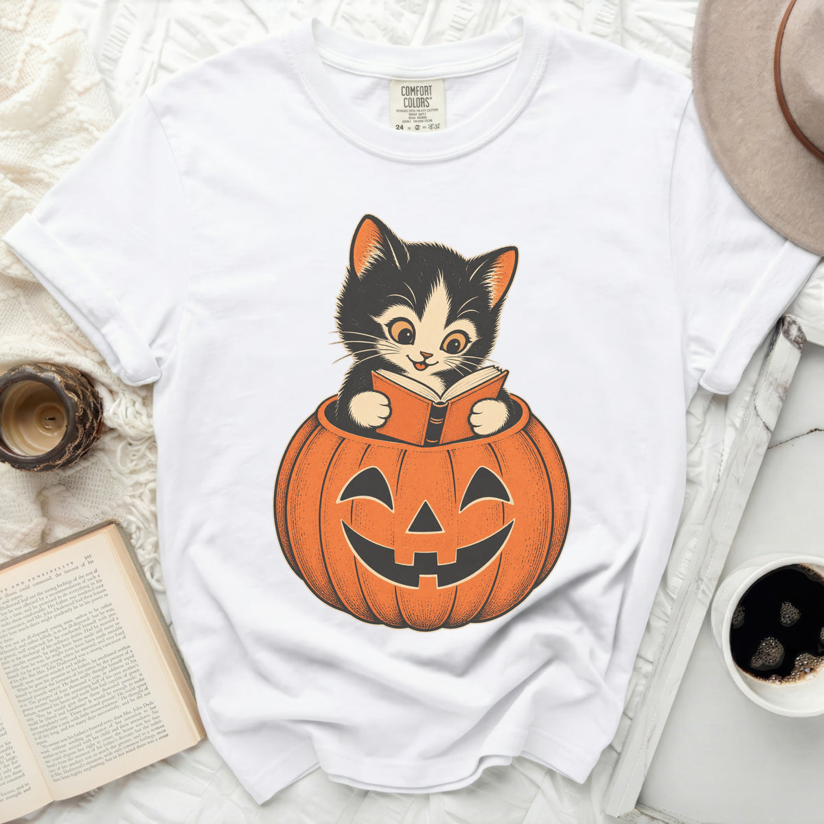 White t-shirt with a graphic of a black kitten reading inside a jack-o'-lantern.