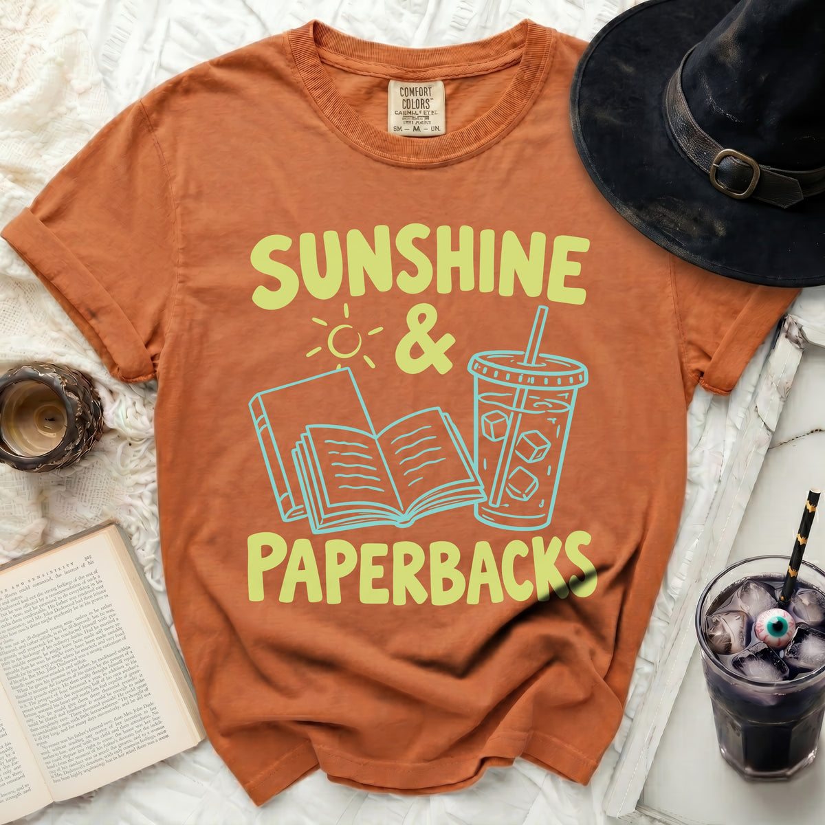 Orange t-shirt with "Sunshine & Paperbacks" graphic, books, and drink.