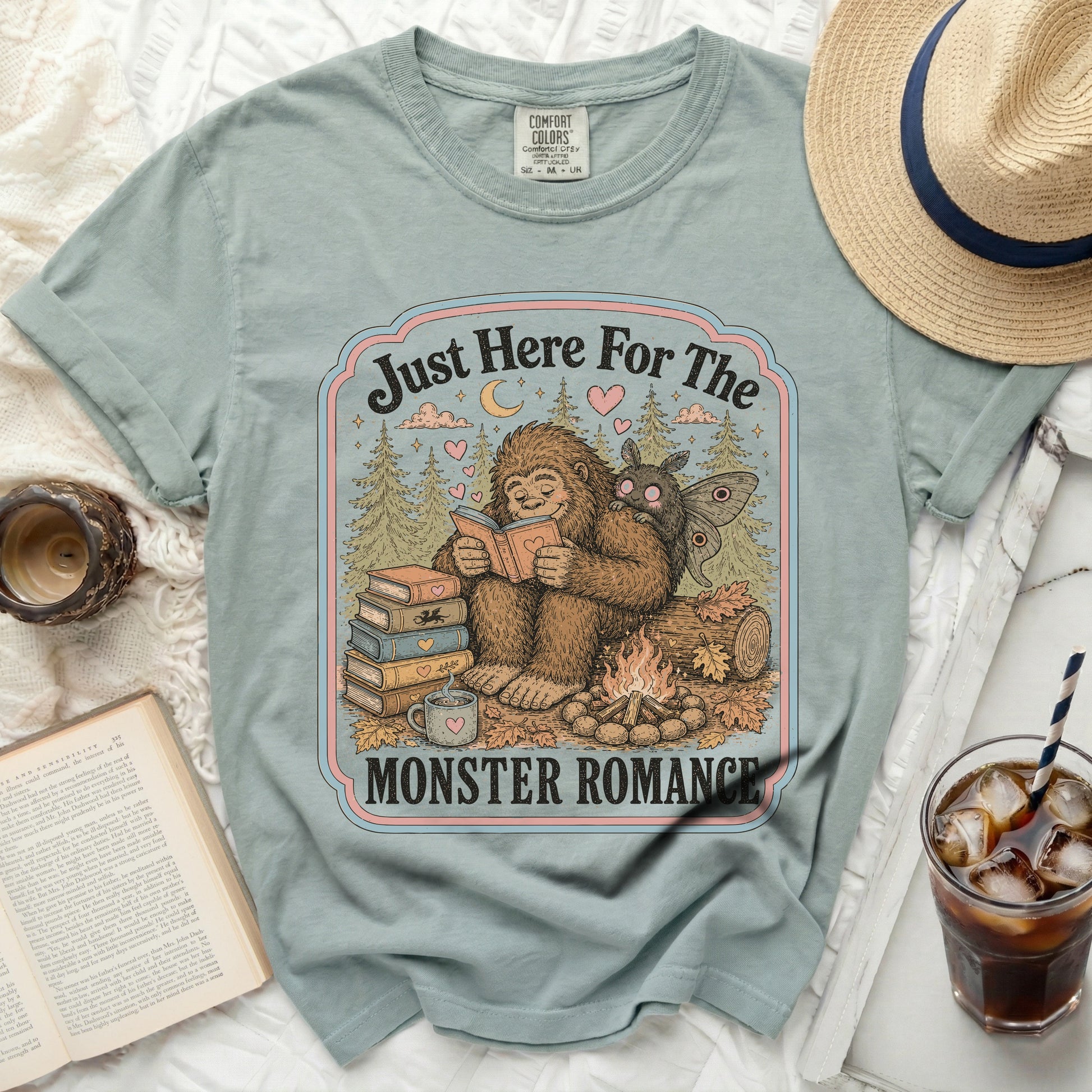 Bigfoot and moth reading by campfire with text "Just Here For The Monster Romance".