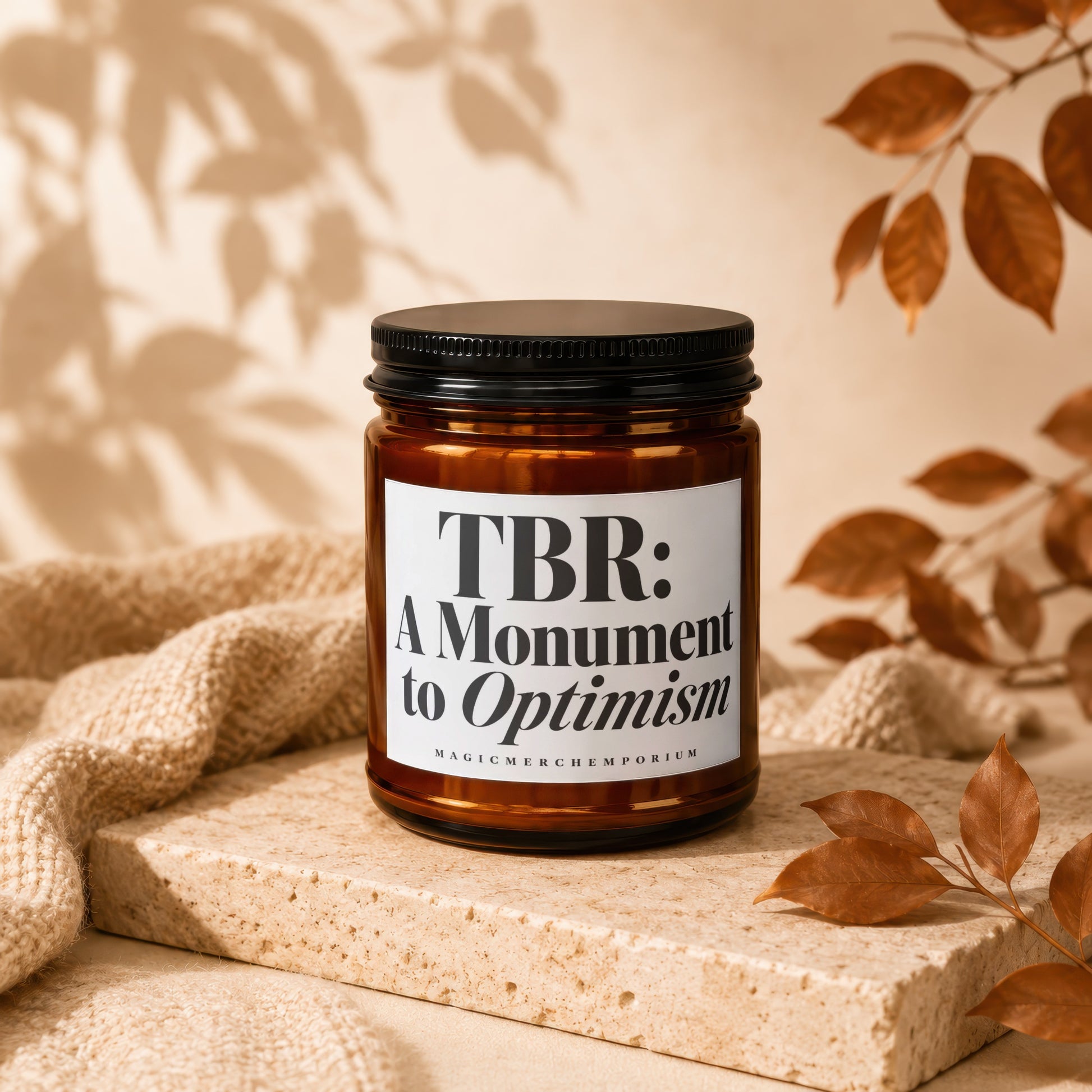 Amber jar candle with black lid, reading "TBR: A Monument to Optimism".
