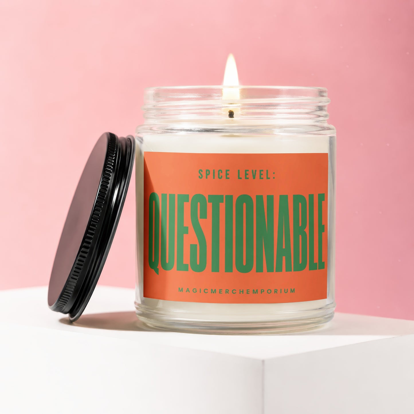 Burning candle in glass jar with black lid open, orange label reads "Spice Level: Questionable".