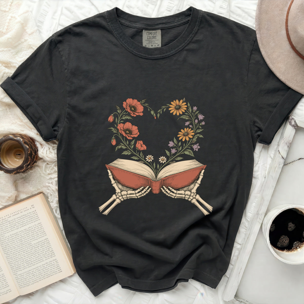Dark t-shirt with skeleton hands holding open book with floral heart design.