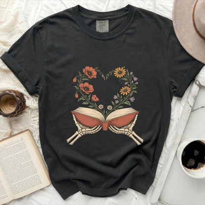 Dark t-shirt with skeleton hands holding open book with floral heart design.