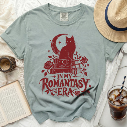Light blue t-shirt with red graphic of a cat on books, moon, and text "IN MY ROMANTASY ERA".