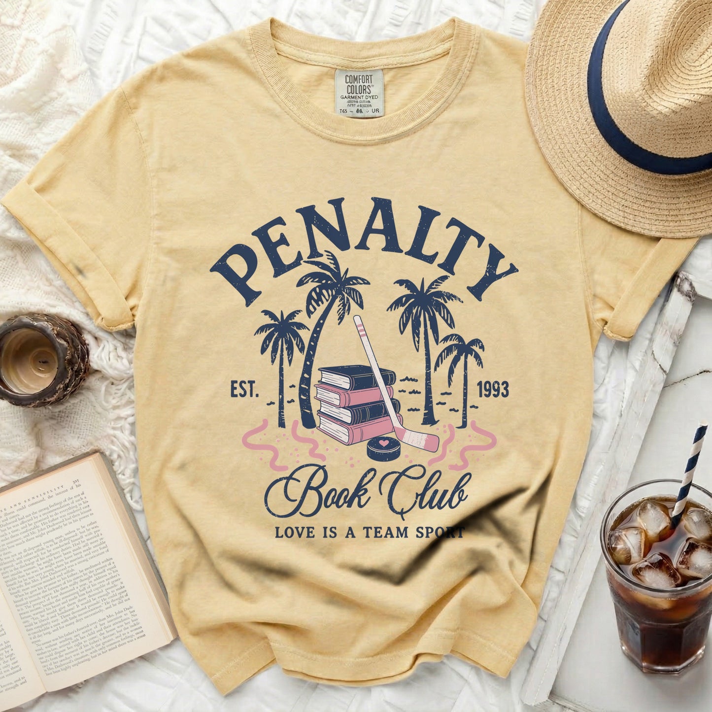 Yellow t-shirt with "Penalty Book Club" text, hockey stick, and palm trees.