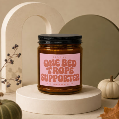 Amber jar candle with black lid labeled "ONE BED TROPE SUPPORTER".