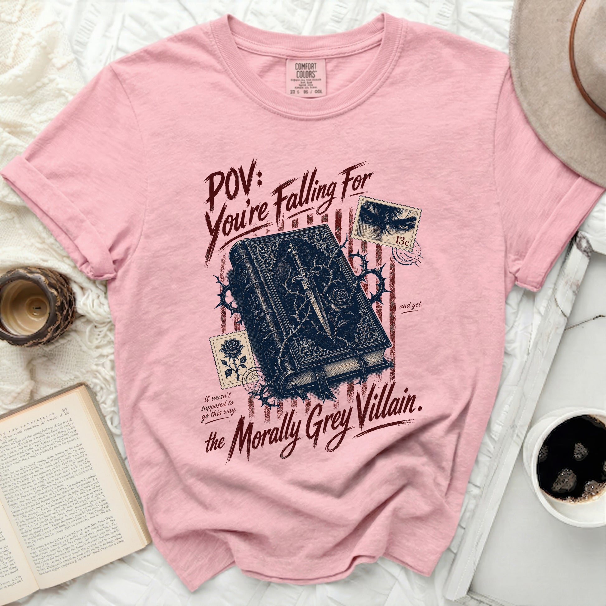 Pink t-shirt with a dark, ornate book and distressed text "POV: You're Falling For the Morally Grey Villain."