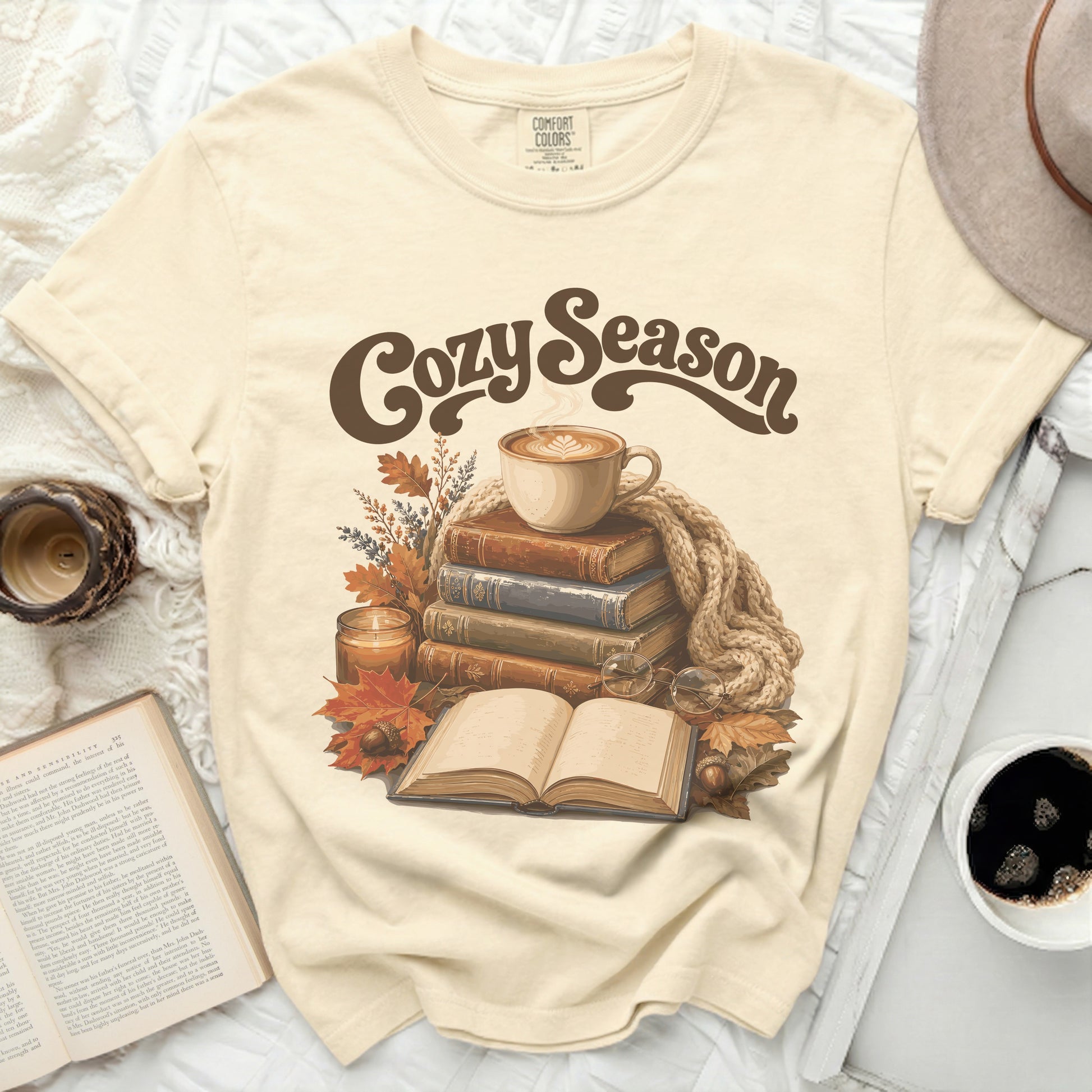 Cream t-shirt with "Cozy Season" graphic, books, coffee, and fall leaves.