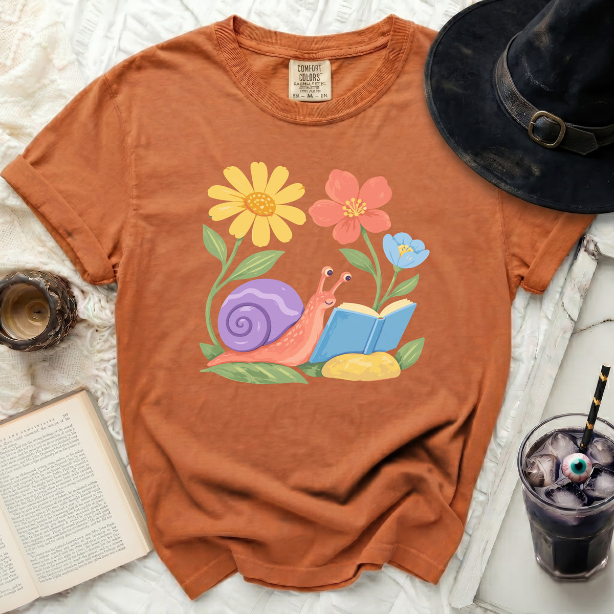 Orange t-shirt with a graphic of a snail reading a book surrounded by flowers.