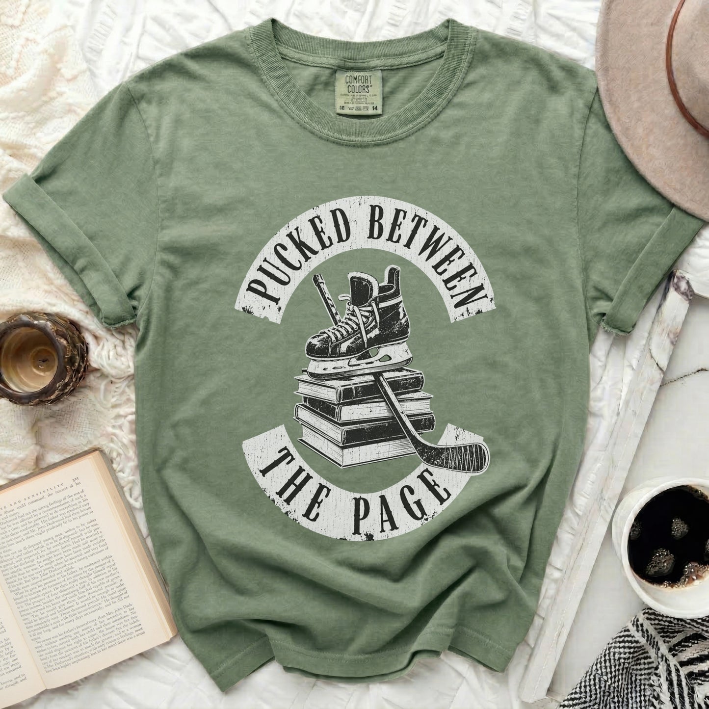 Green t-shirt with "Pucked Between The Page" text and hockey gear.