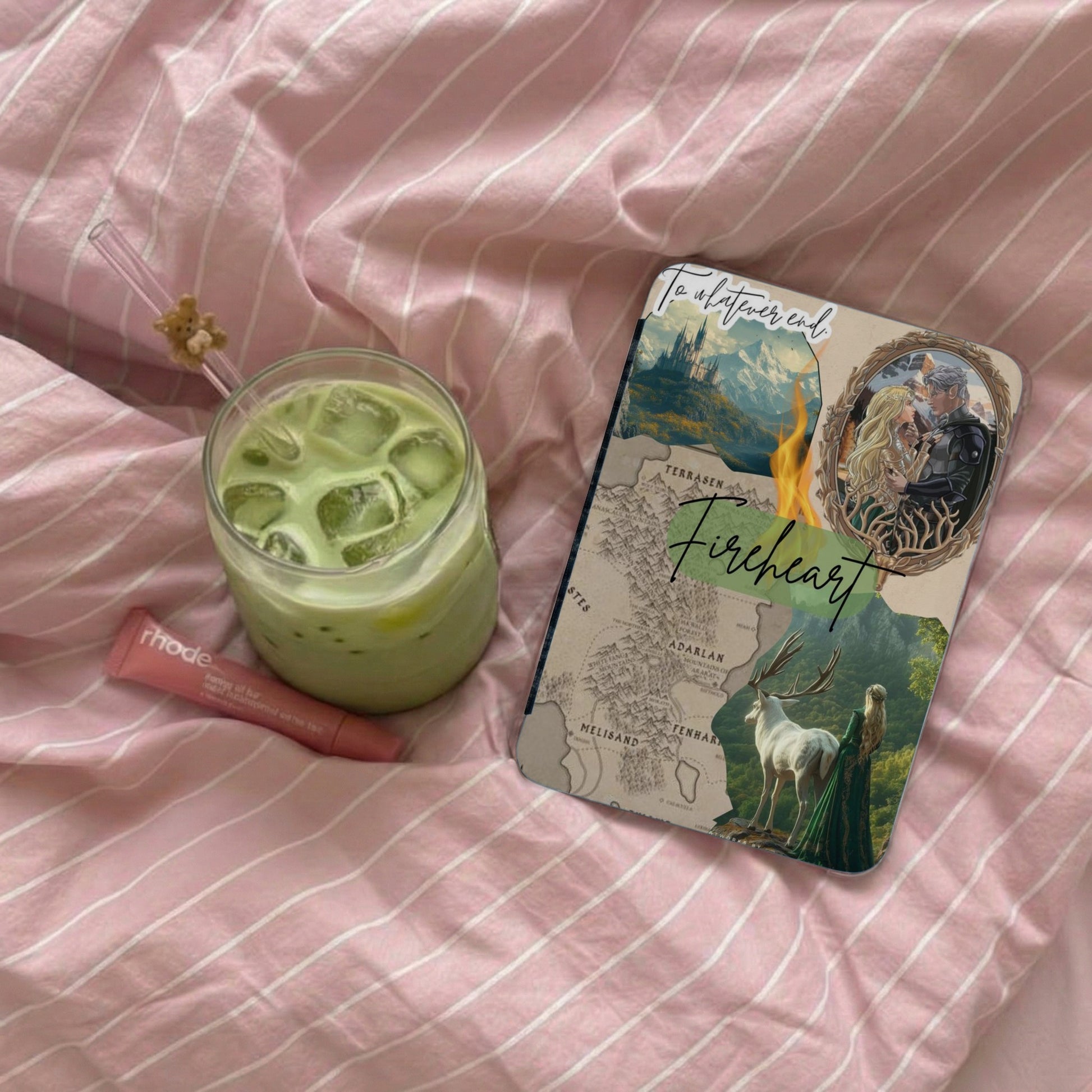 Notebook with fantasy art, map, and "Fireheart" title, next to matcha drink and lip balm.