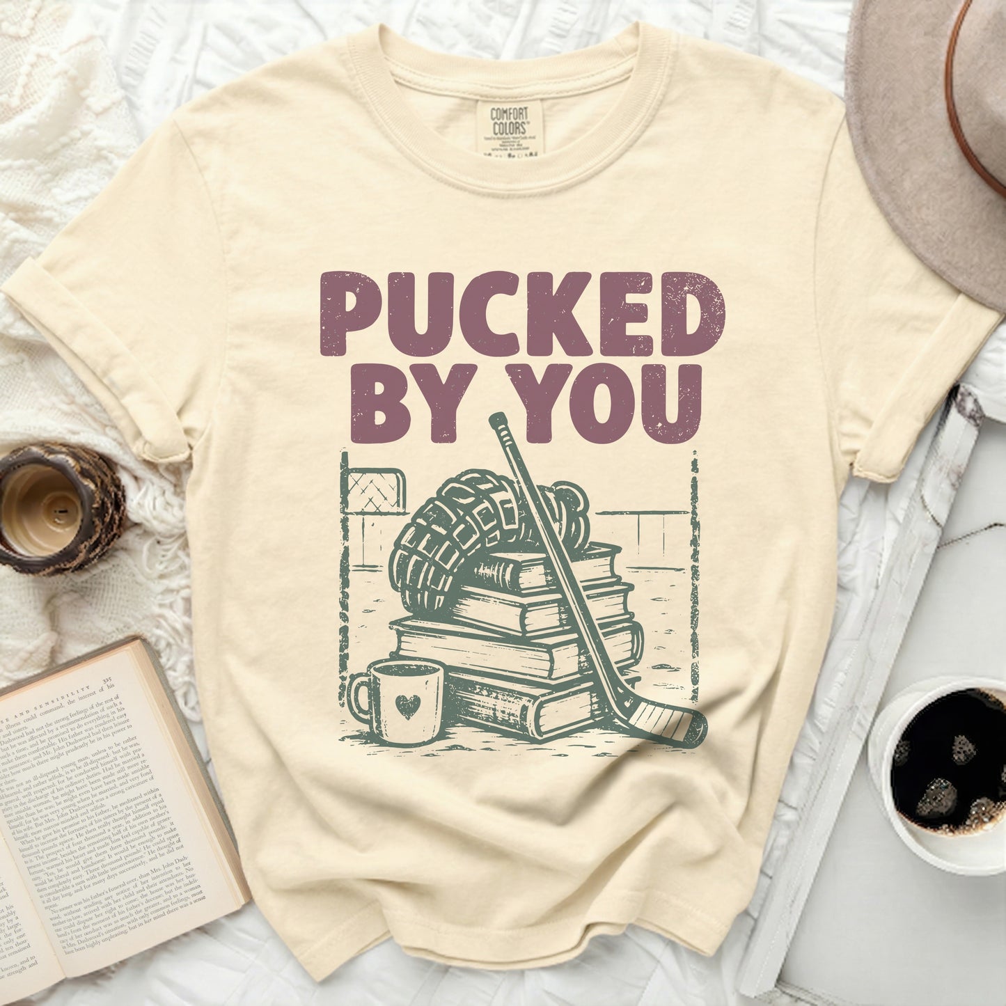 Cream t-shirt with "Pucked By You" text and hockey gear illustration.