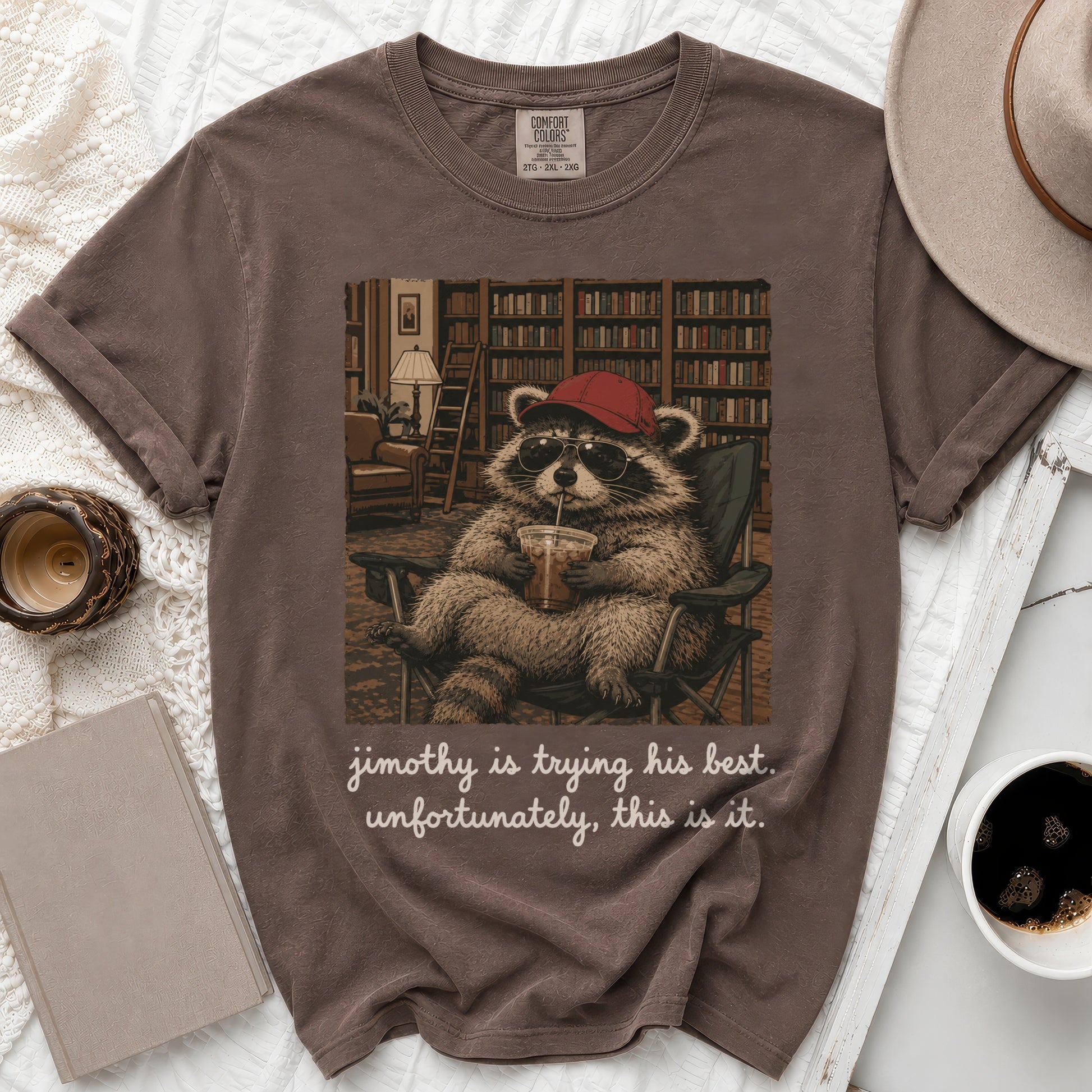Brown t-shirt with graphic of raccoon wearing sunglasses and hat, drinking.