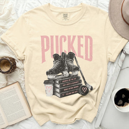 Cream t-shirt with "Pucked" text, hockey skates, puck, and books.